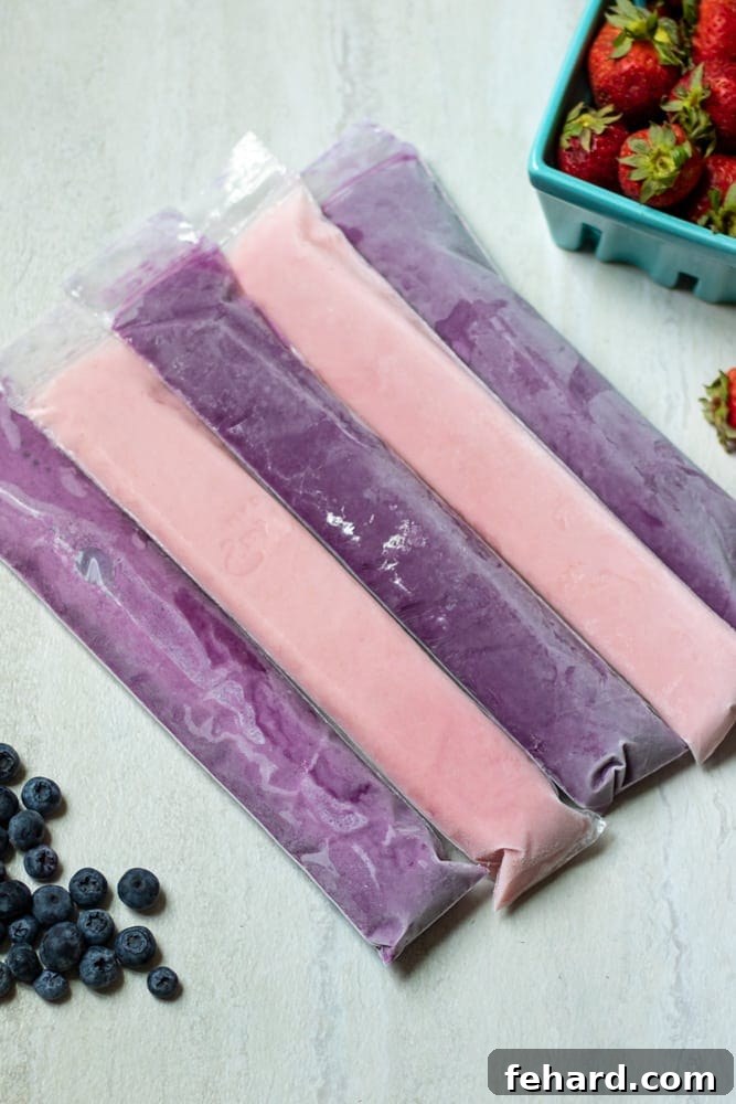 Vibrant homemade yogurt tubes filled with berry goodness, displayed alongside fresh strawberries and blueberries, ready for a healthy snack.