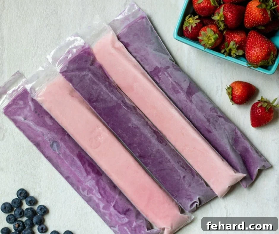 A delightful arrangement of five vibrant homemade berry yogurt tubes, positioned invitingly next to a scattering of fresh blueberries and strawberries, ready to be stored or enjoyed.
