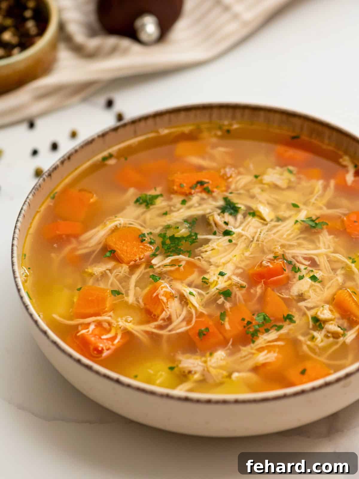 Bowl of homemade chicken soup filled with shredded chicken and tender potatoes and carrots topped with fresh parsley.