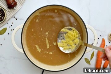 Strainer spoon scooping off fat solids from homemade chicken soup broth.
