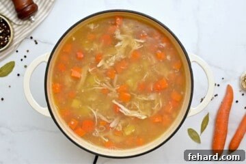 Chicken soup cooked in a large soup pan with carrots, potatoes, and sweet potatoes.