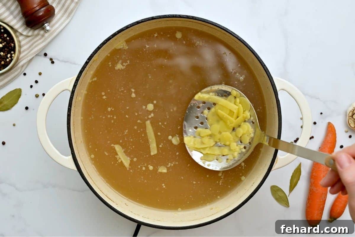 Strainer spoon scooping off fat solids from homemade chicken soup broth.