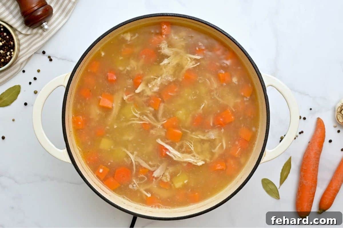 Chicken soup cooked in a large soup pan with carrots, potatoes, and sweet potatoes.