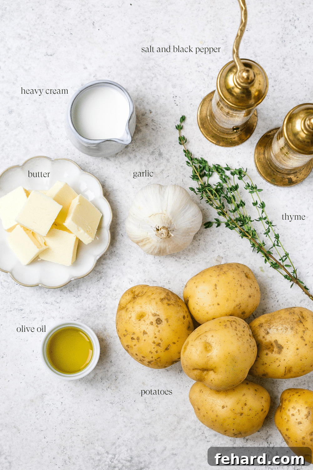 A vibrant flat lay showcasing all the fresh ingredients needed for roasted garlic mashed potatoes: a whole garlic head, golden potatoes, fresh thyme, a stick of butter, and a bottle of olive oil.