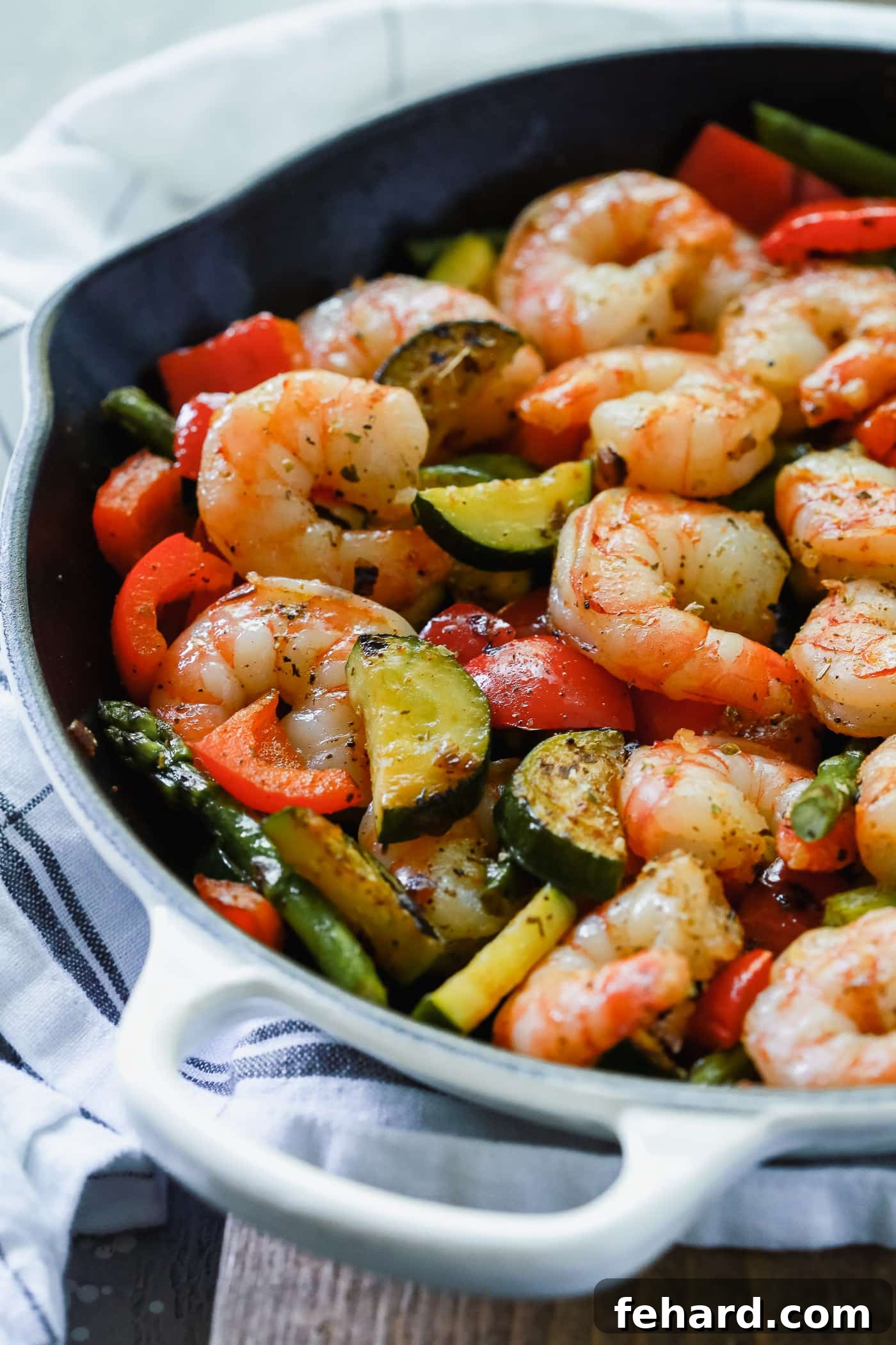 Overhead view of a cast iron with shrimp, bell peppers, zucchini, and asparagus. 