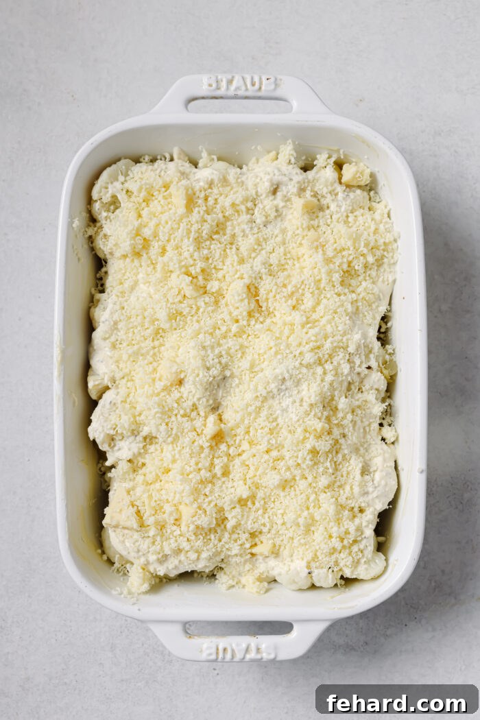 Shredded cheese sprinkled over the cauliflower and cream sauce in a baking dish.