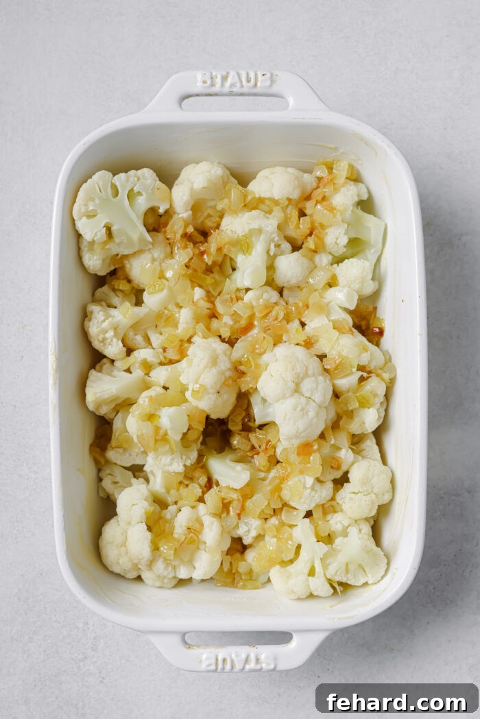 Cooked cauliflower florets arranged in a greased baking dish, topped with caramelized onions.