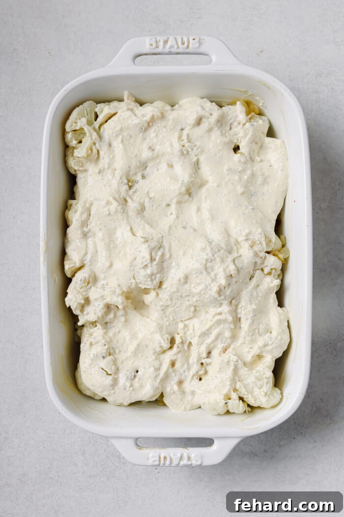 Cauliflower with cream cheese sauce poured over it in a white casserole dish.