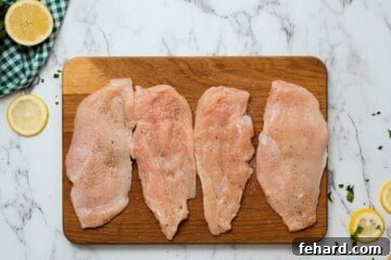 Zesty Honey-Glazed Skillet Chicken 4 Thin chicken cutlets on wooden cutting board seasoned with salt and pepper and fresh lemon slices in background.
