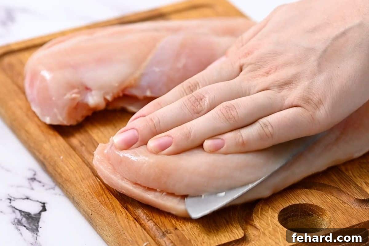 How to Make Chicken Cutlets A knife slicing a thick chicken breast horizontally to create thinner chicken cutlets.