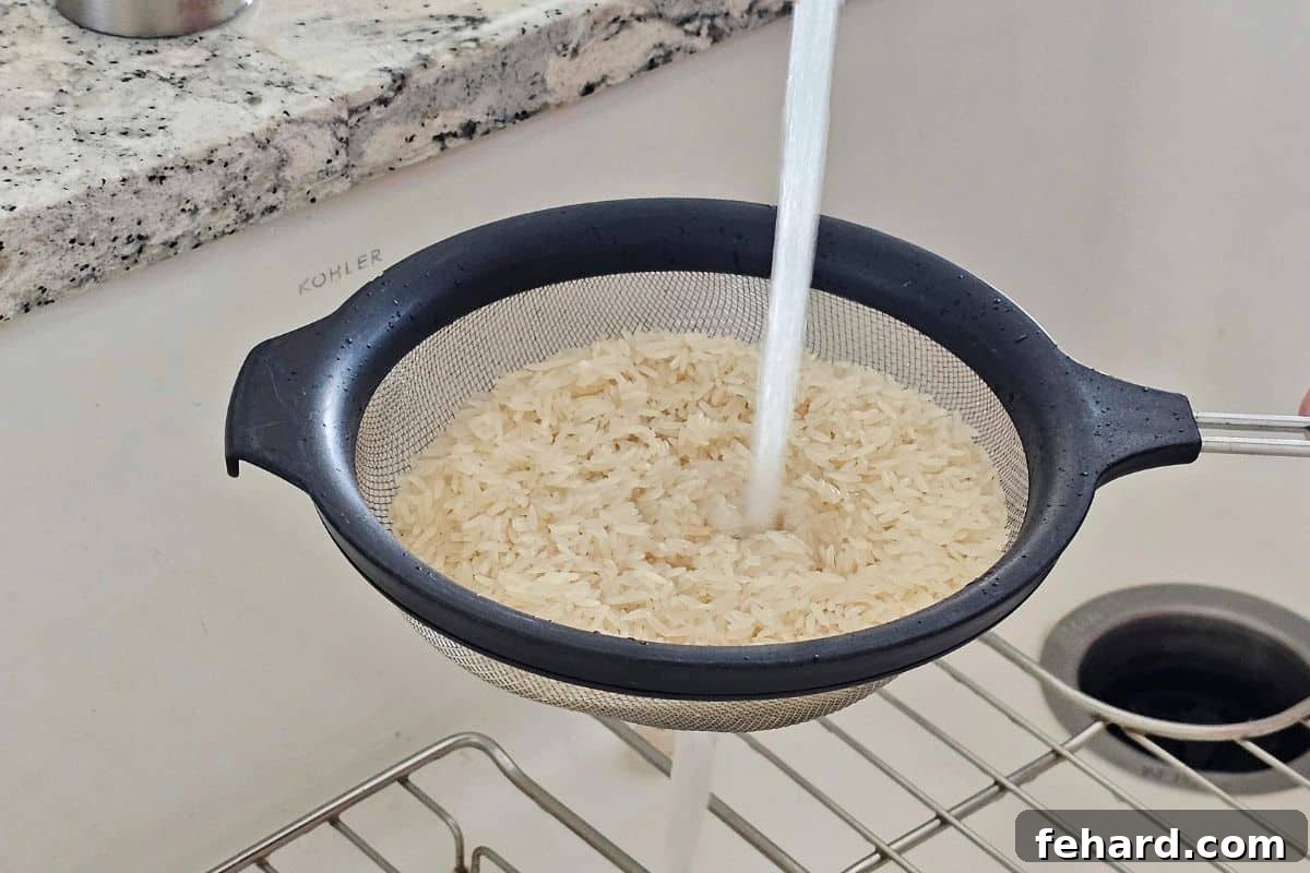 Long grain white rice in a fine mesh strainer being rinsed under cold tap water to remove excess starch.