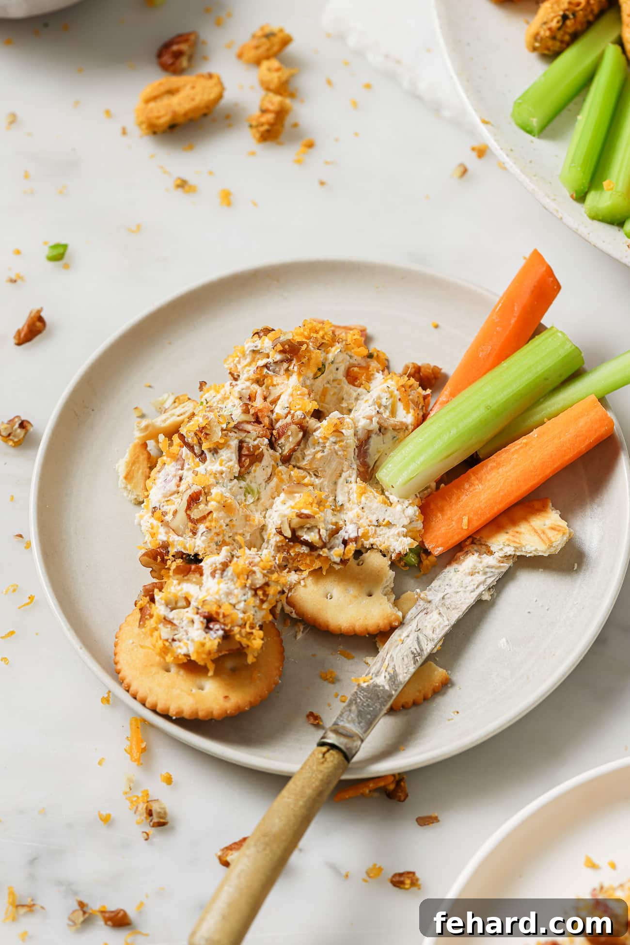 A cheese ball serving on a plate with vegetables and crackers. 