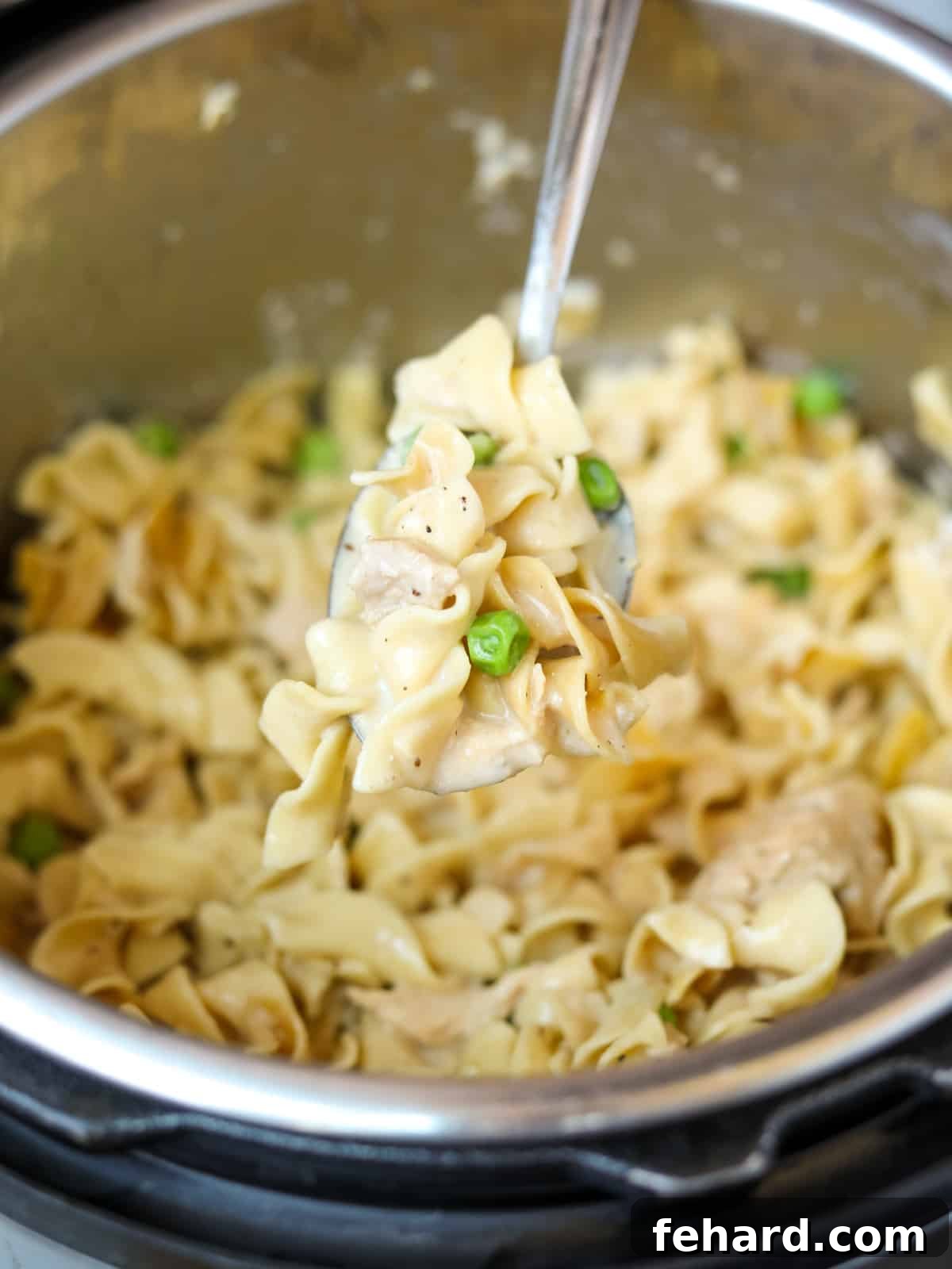 A spoon emerging from an Instant Pot, laden with tender egg noodles, flaky tuna, and vibrant green peas, showcasing the creamy texture of the casserole.