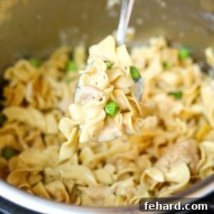 A spoonful of creamy tuna noodle casserole being lifted from the Instant Pot, showing the perfect blend of noodles, tuna, and peas.