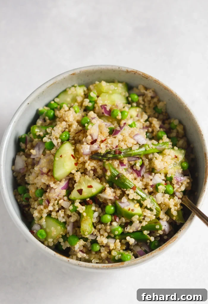Overhead view of Spring Quinoa Salad with dressing being poured over fresh vegetables and quinoa.