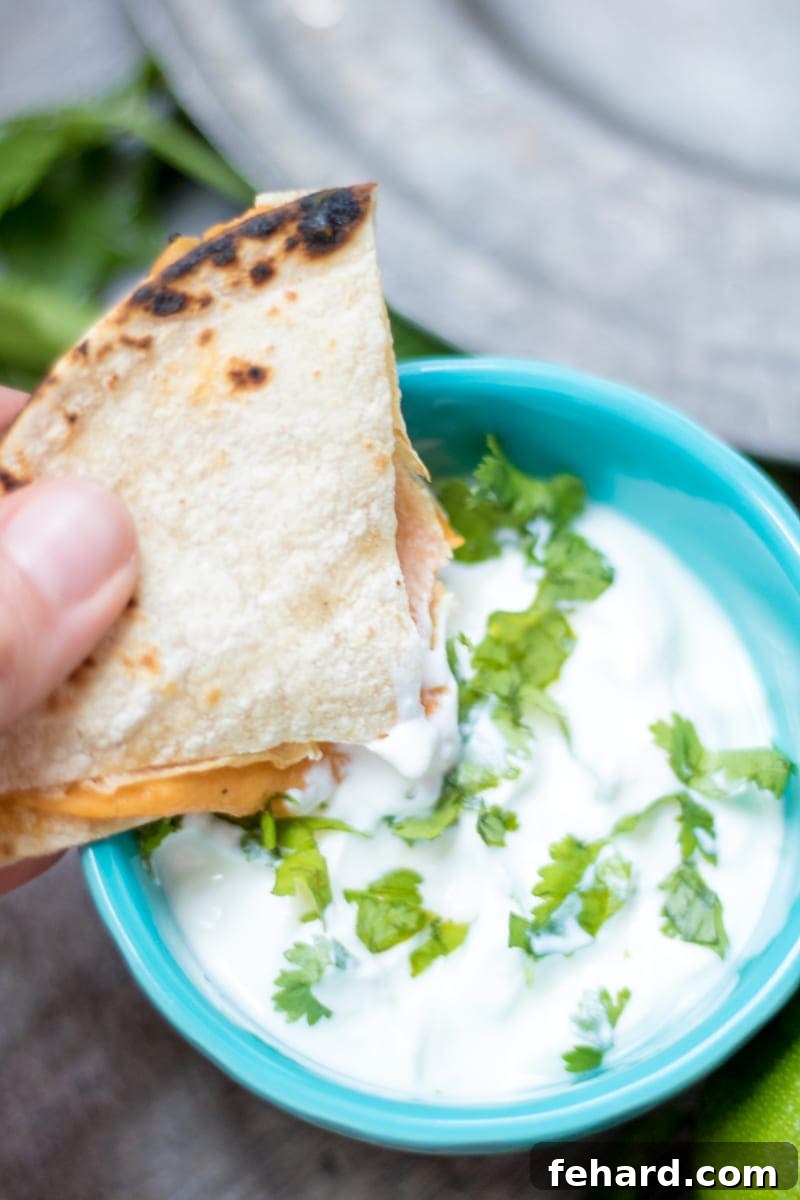 Guilt-Free Cheese Quesadilla 3 A healthy hidden veggie quesadilla wedge being dipped into a creamy cilantro sour cream sauce, showcasing the golden-brown tortilla and inviting texture.
