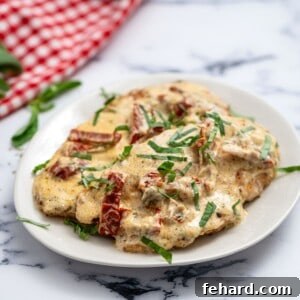 Chicken cutlets on white plate with parmesan cream and sun-dried tomato sauce.