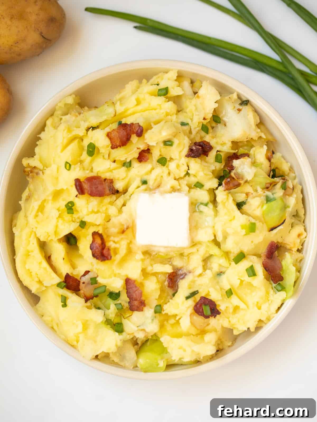 Colcannon in a beautiful serving dish, topped with a melting pat of butter and garnished with crispy bacon bits and fresh green onions.