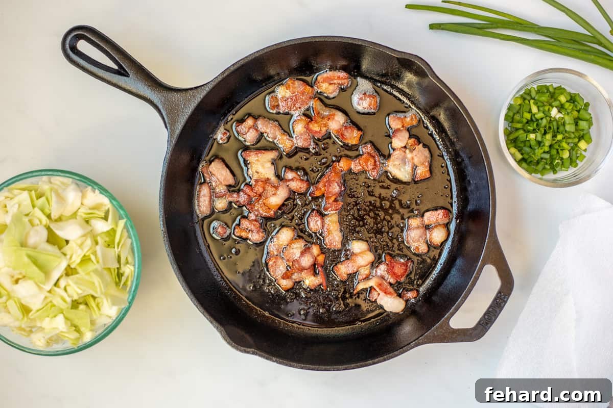Crispy bacon in a skillet, with chopped cabbage waiting to be sautéed in the rendered drippings.