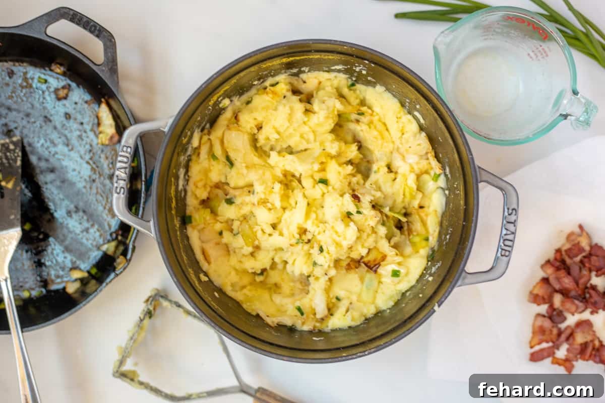 Mashed potatoes mixed with sautéed cabbage, green onions, and bacon inside a large Dutch oven skillet, ready to be served.