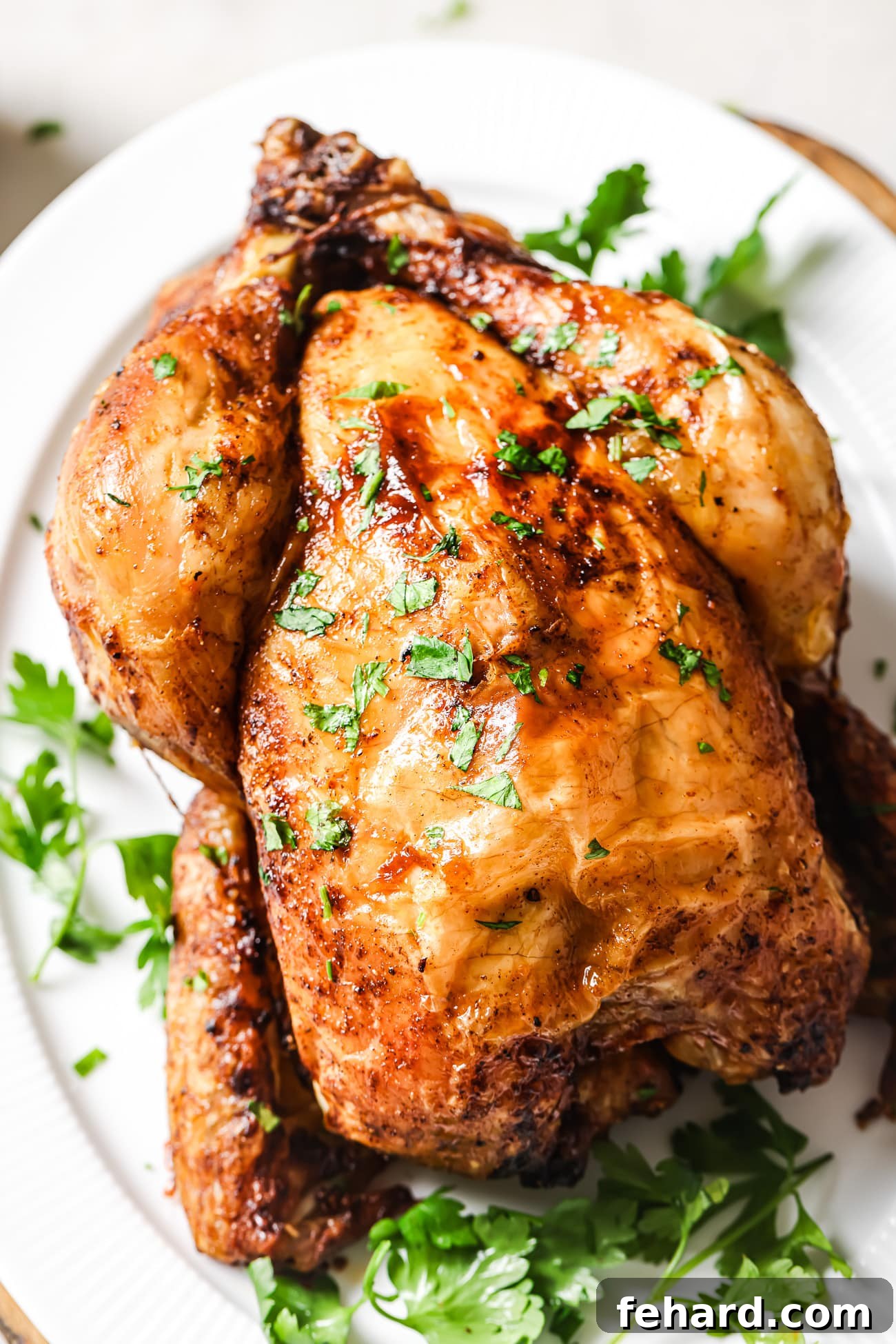 Air Fryer Whole Chicken on a white platter with chopped parsley on top, garnished and ready to serve.