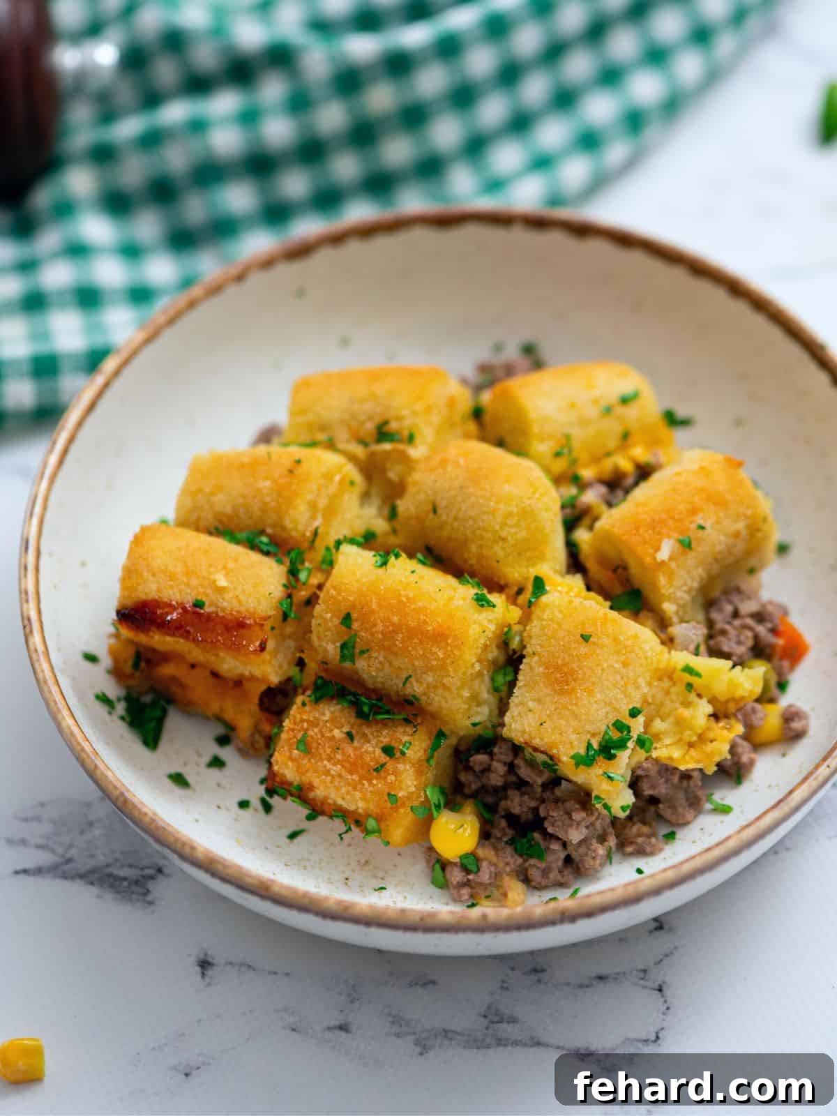 A serving of Tater Tot Casserole in a white bowl, garnished with fresh herbs, showcasing the crispy tater tots and rich filling.