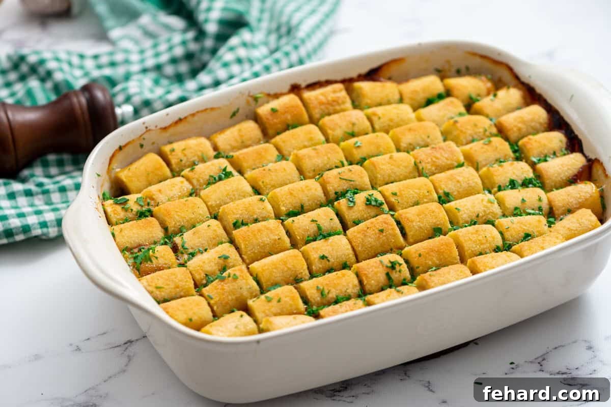 A baked Tater Tot Casserole in a white baking dish, freshly removed from the oven and garnished with fresh parsley.
