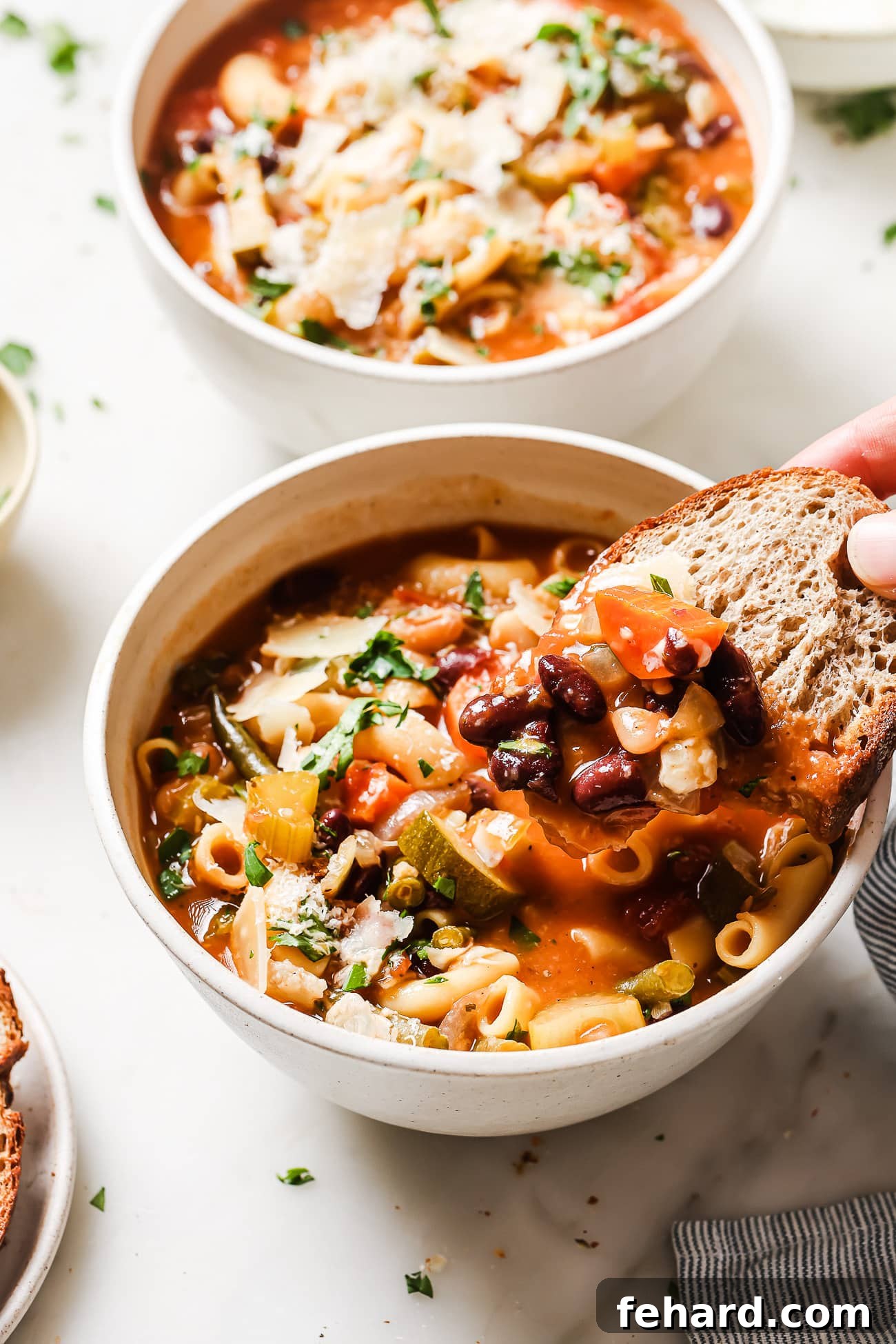 Hearty Vegetable Minestrone 7 A bowl of Minestrone Soup with a slice of fresh, crusty bread dipped into the flavorful broth, invitingly close.