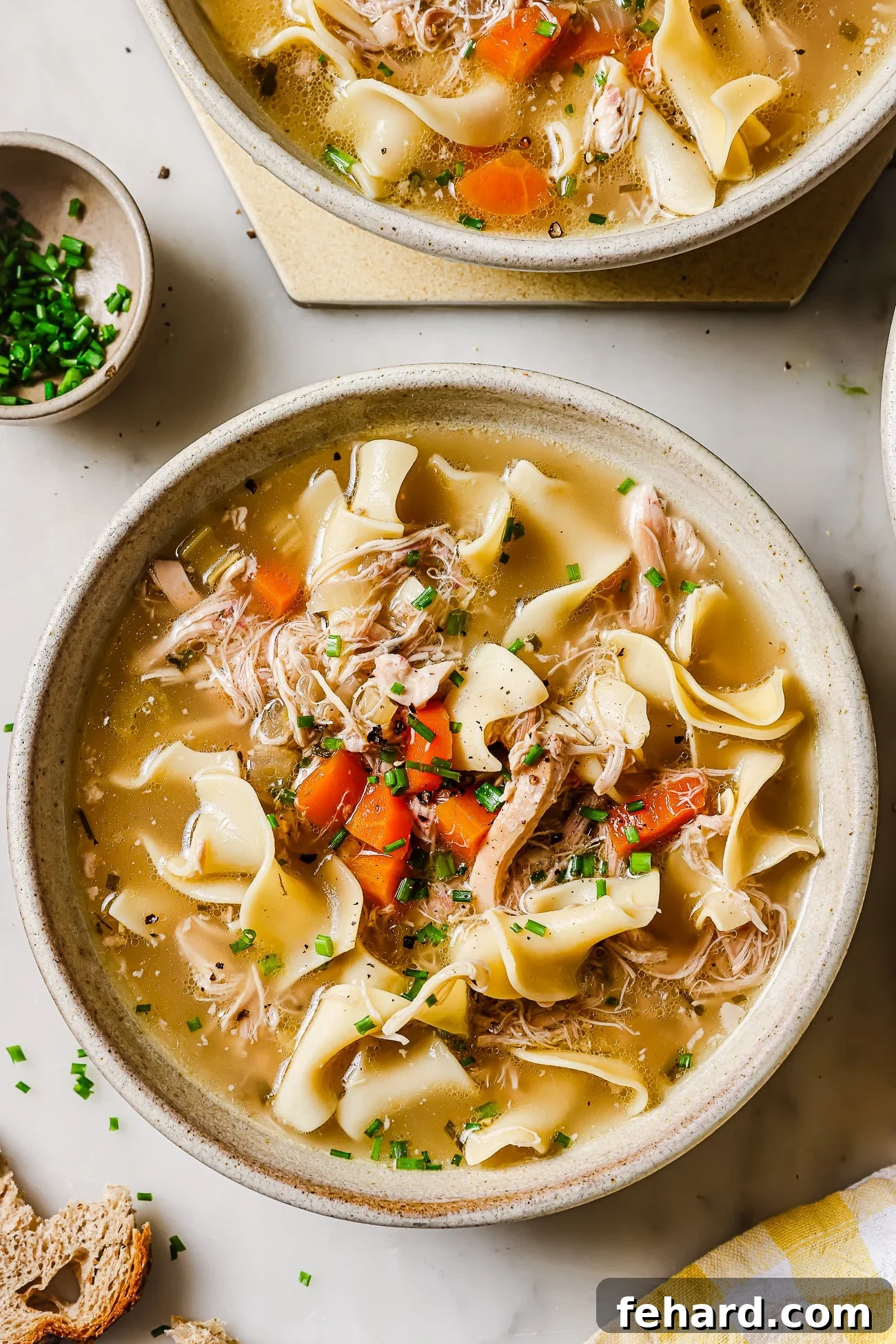 A bowl of slow cooker chicken noodles garnished with chives, ready to be served.