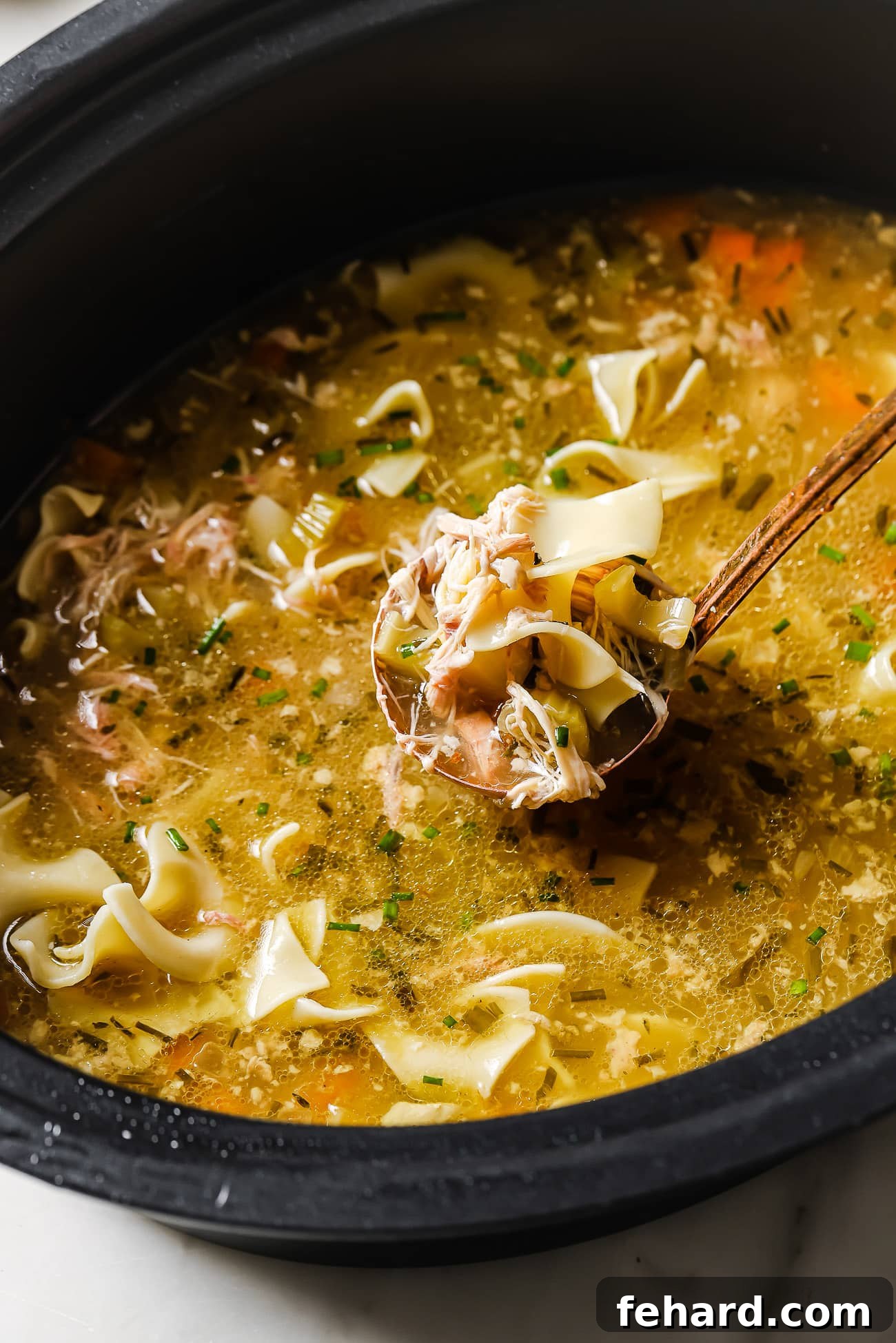 A closeup of slow cooker chicken noodles with a ladle of soup, ready to be served.