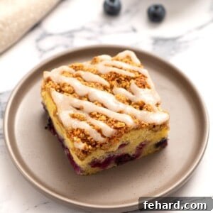 Slice of blueberry Coffee Cake on a gray plate drizzled with lemon glaze.