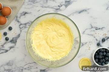 Creamed butter, sugar, eggs, sour cream, and lemon zest in a large mixing bowl for the cake batter, with fresh blueberries nearby.