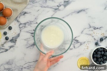 Powdered sugar and lemon juice being whisked together in a small mixing bowl to create a smooth glaze, with fresh blueberries and lemons in the background.