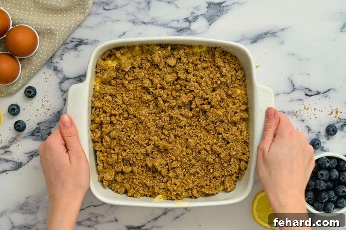 Unbaked Lemon Blueberry Coffee Cake layered with batter and streusel topping in a white square baking dish, ready for the oven.