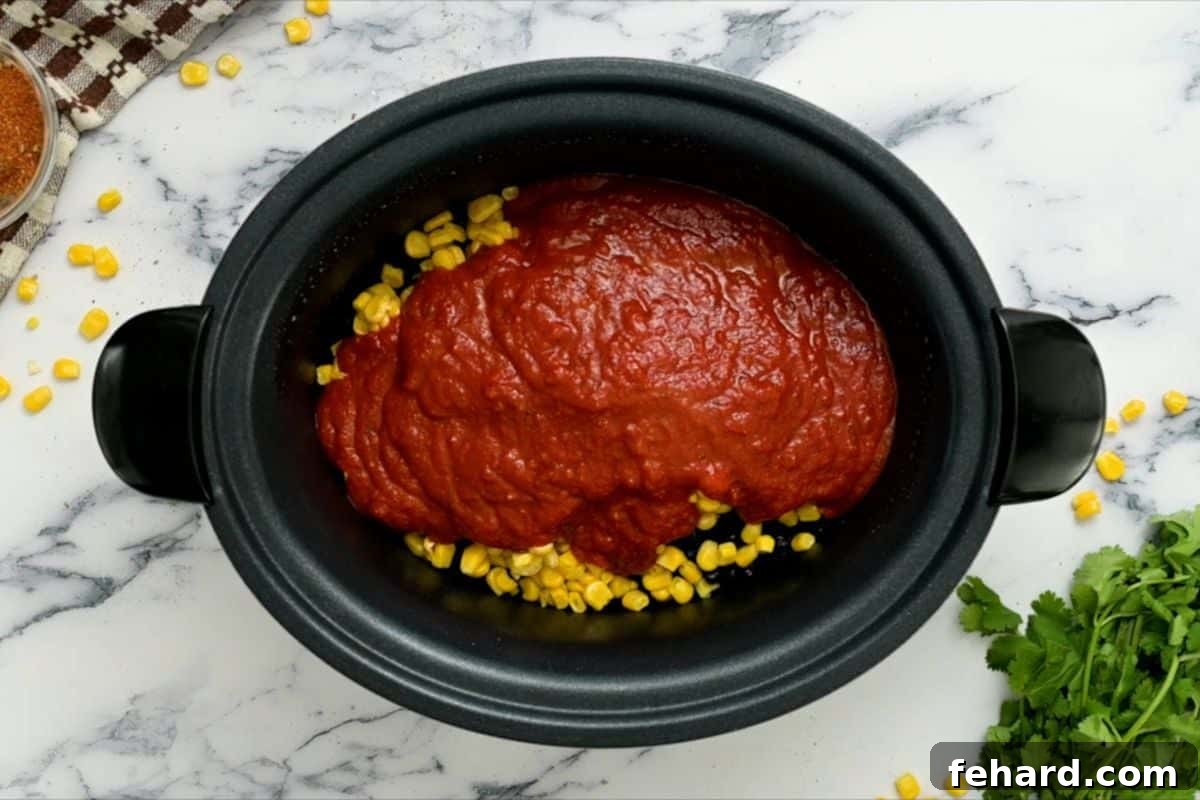 Seasoned chicken breasts, corn, black beans, and salsa layered in a crockpot, showing the assembly process for delicious slow cooker salsa chicken.