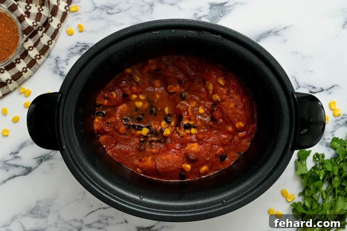 Slow cooker with perfectly cooked chicken breasts, beans, and corn, all covered with rich salsa, ready for shredding.
