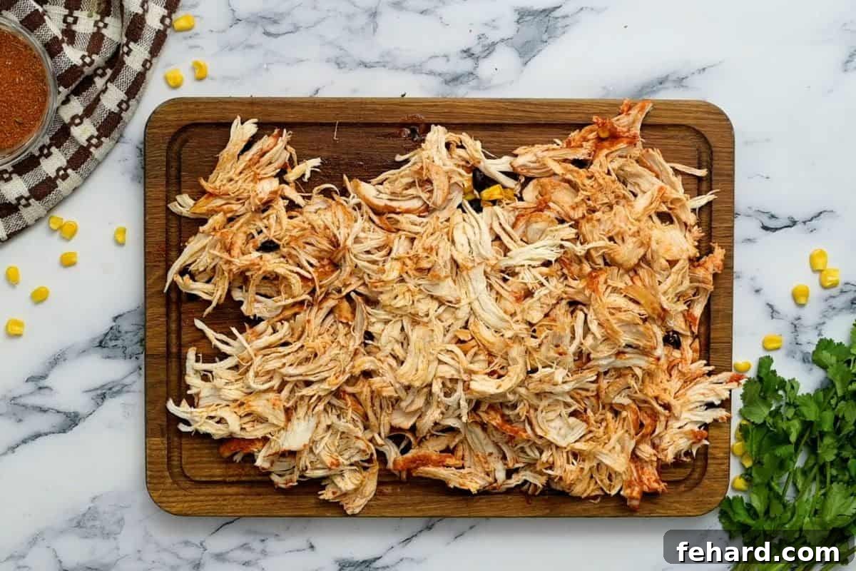 Perfectly shredded chicken on a cutting board, moist and ready to be returned to the slow cooker for final steps.