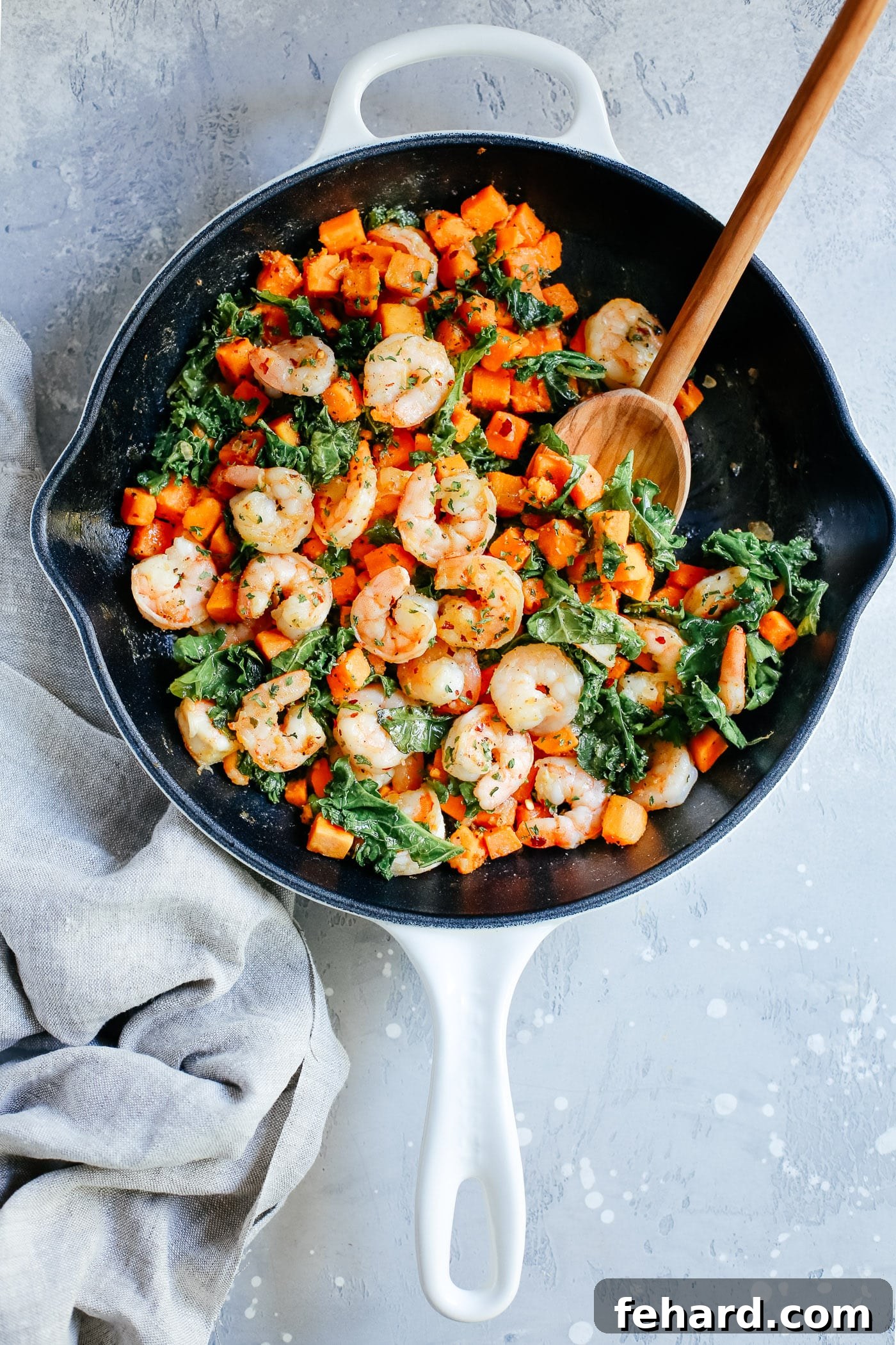 Overhead view of a white skillet featuring perfectly cooked shrimp, tender sweet potato, and fresh kale