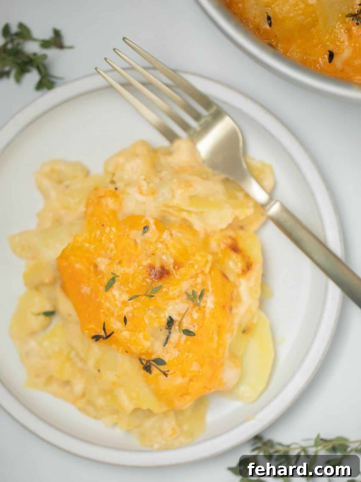 Instant Pot Scalloped Potatoes - Creamy & Easy Instant Pot Scalloped Potatoes dished out on plate topped with fresh thyme.