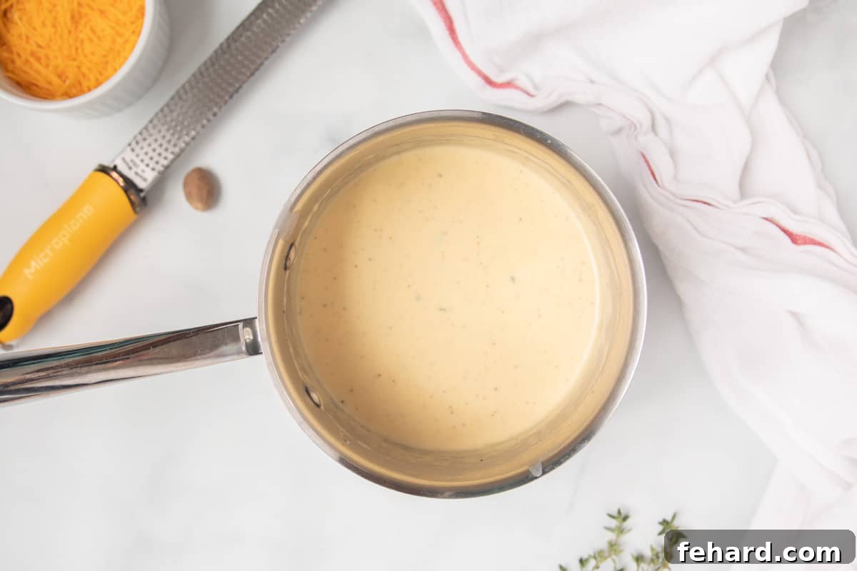 Instant Pot Cheesy Scalloped Potatoes Cream Sauce Cream Sauce inside saucepan next to fresh thyme and nutmeg bulb.