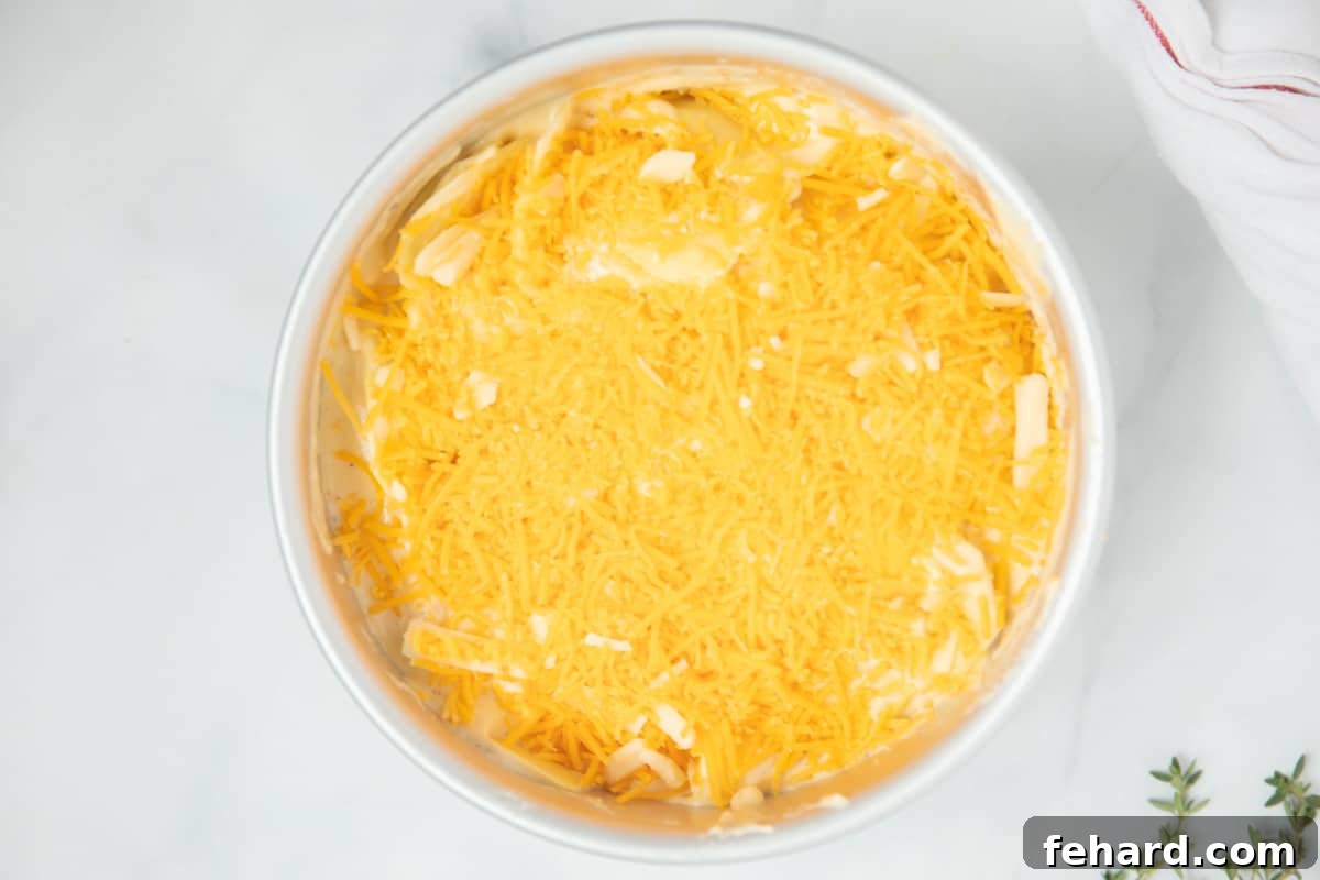 Instapot Cheesy Scalloped Potato Recipe Assembly Sliced potatoes, cream sauce, and cheese layered in cake pan safe for pressure cooker.