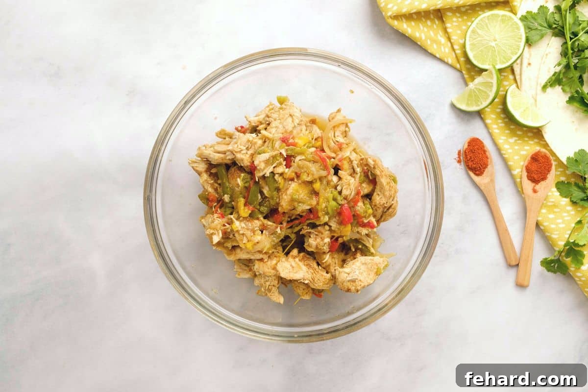 Cooked chicken and pepper mixture in a mixing bowl with fresh lime zest sprinkled over it.