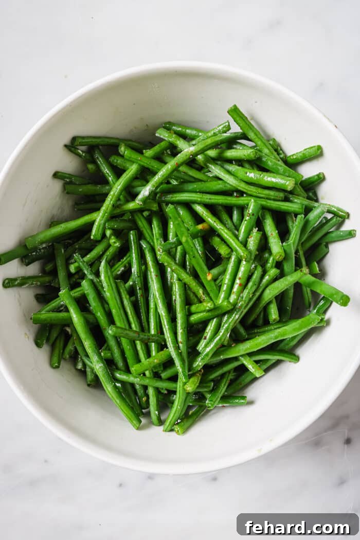 Crispy Air Fried Green Beans 4 Green beans tossed with olive oil, salt, and pepper in a white bowl.