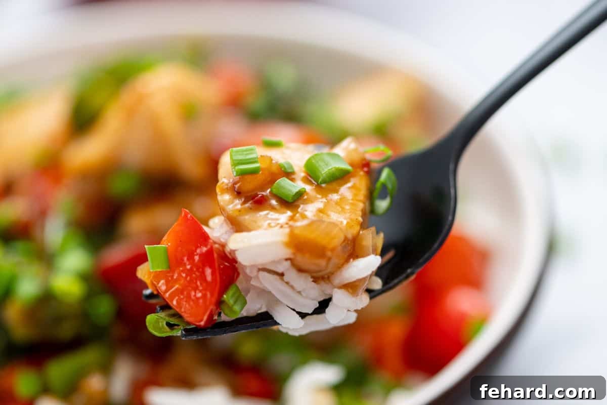 Easy Hunan Chicken Recipe A fork lifts a serving of Hunan Chicken and rice from a bowl, highlighting the tender chicken and savory sauce.
