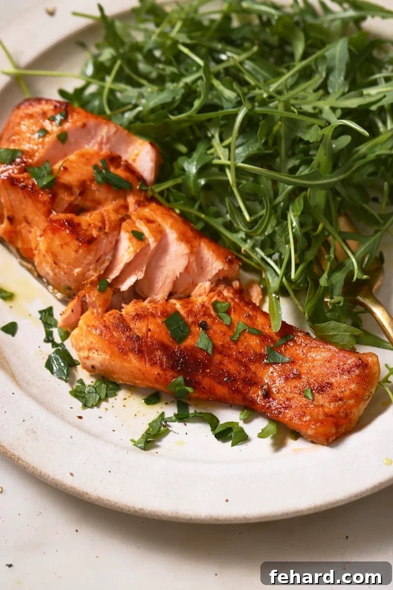 An air fryer trout fillet flaked apart on a white plate, served alongside a fresh green salad.