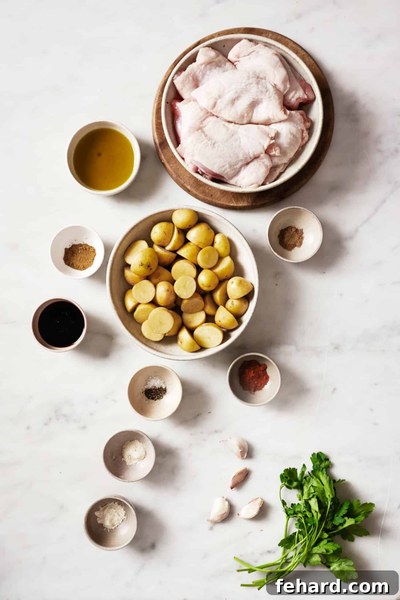 One-Pan Garlic Herb Chicken and Potatoes 3 A selection of fresh ingredients laid out, including chicken thighs, baby potatoes, olive oil, balsamic vinegar, garlic, and various spices in small bowls.