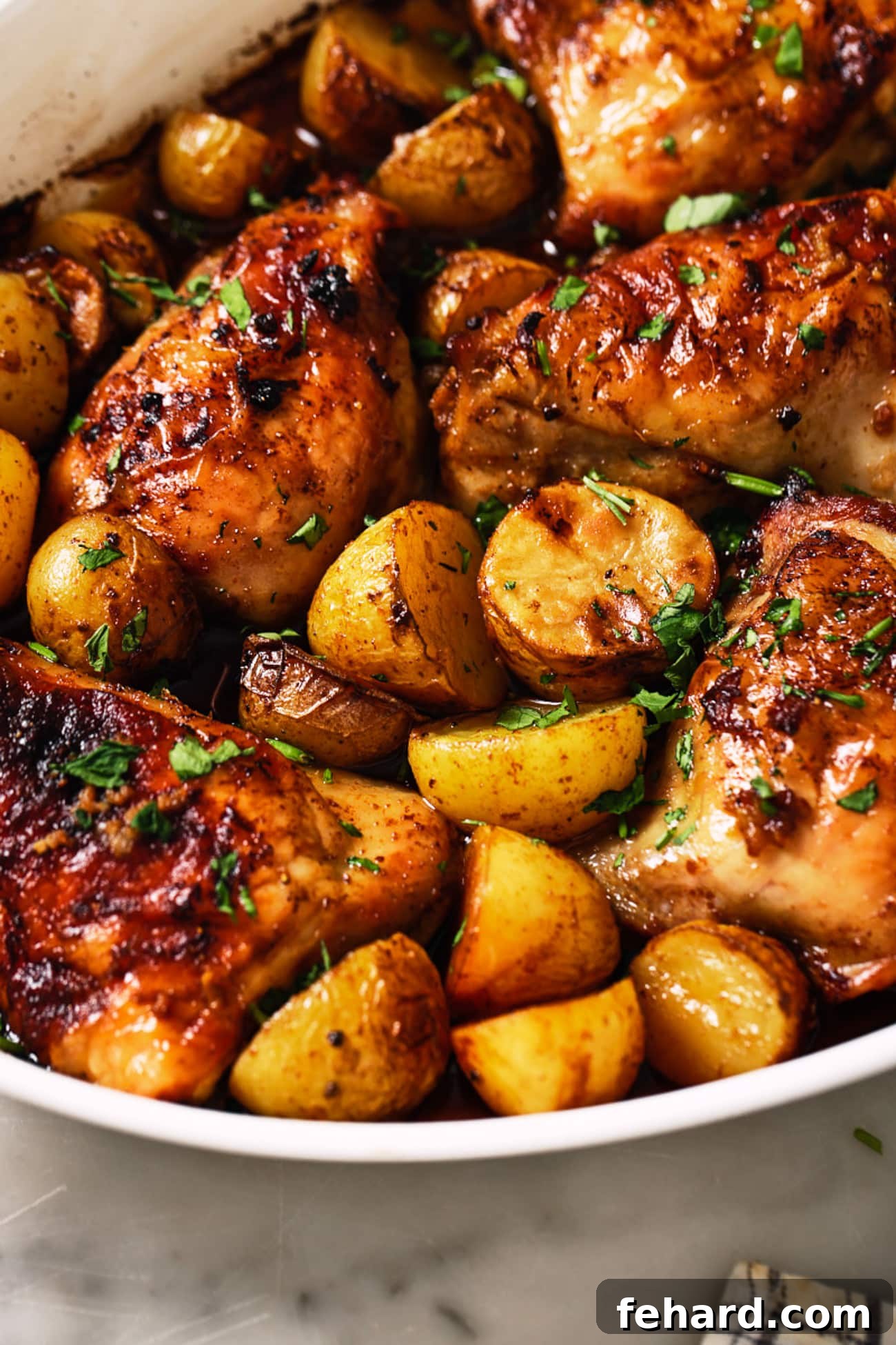 One-Pan Garlic Herb Chicken and Potatoes 6 Close-up of golden-brown chicken thighs and roasted potatoes in a rustic white dish, ready to eat.
