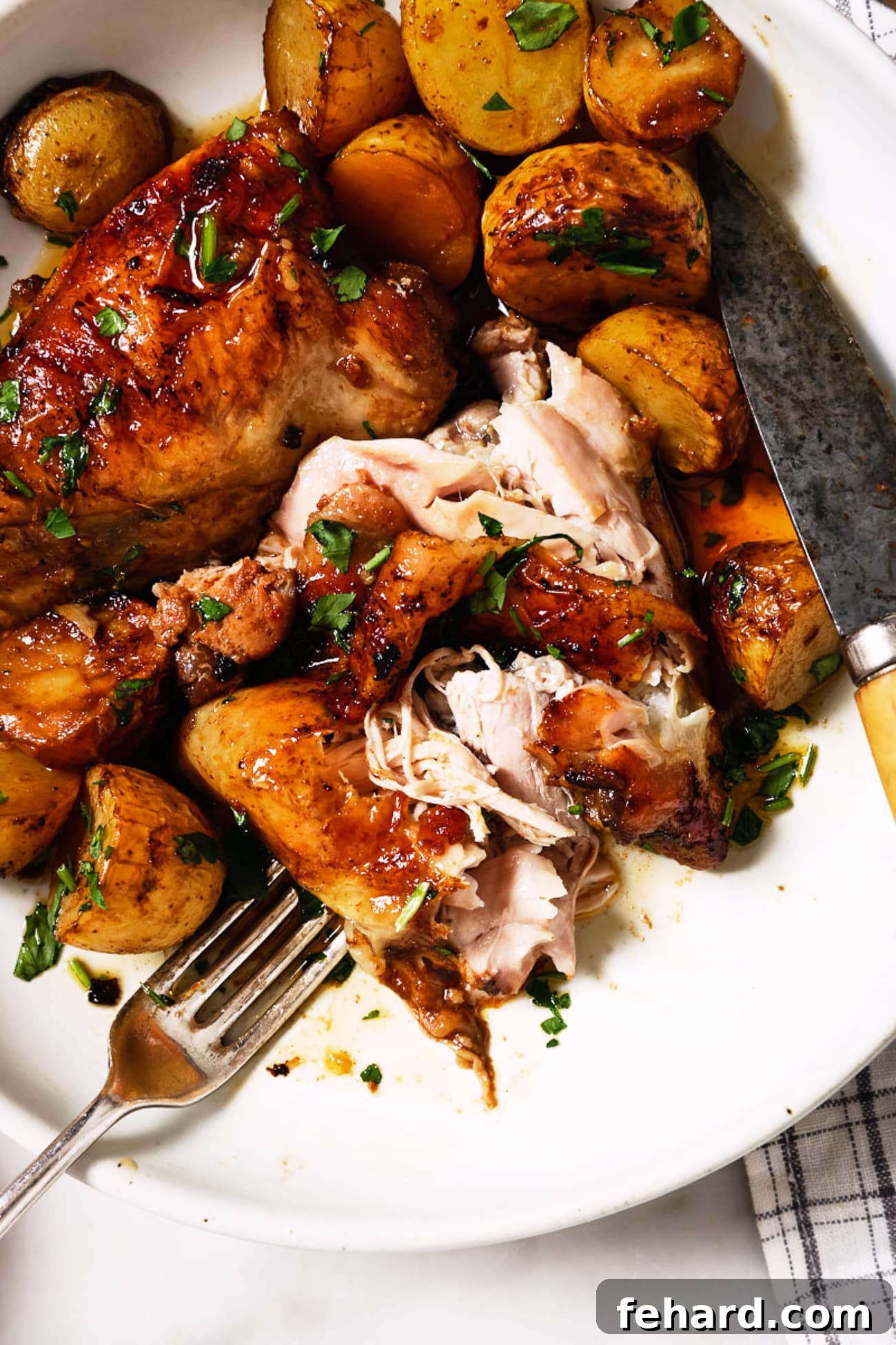 One-Pan Garlic Herb Chicken and Potatoes 8 A plated serving of roasted chicken thighs and potatoes, accompanied by a fork and knife, showcasing the perfect golden-brown crispness.