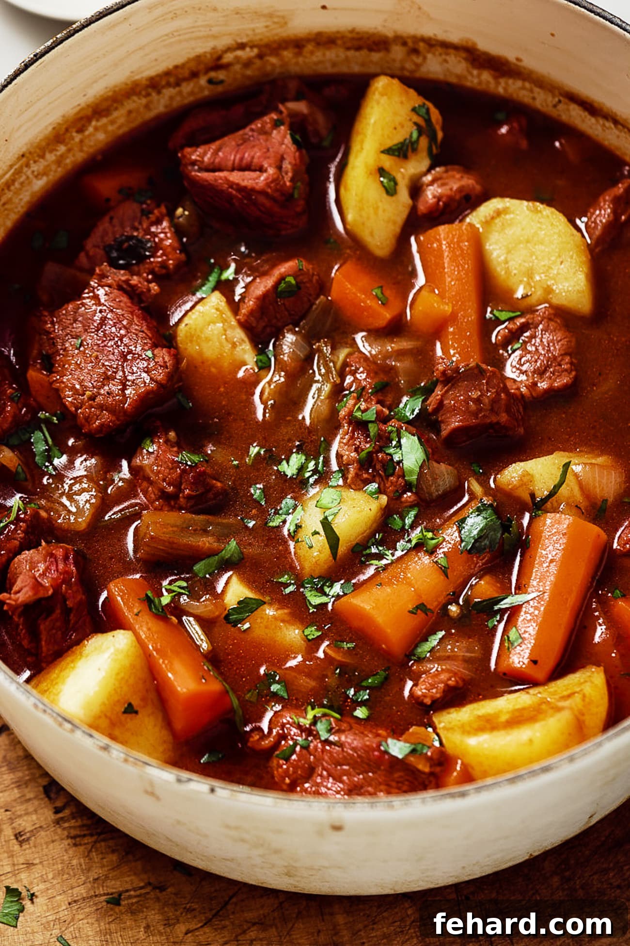 Close-up of a steaming bowl of Guinness beef stew, generously garnished with fresh parsley, highlighting its rich texture and inviting warmth.
