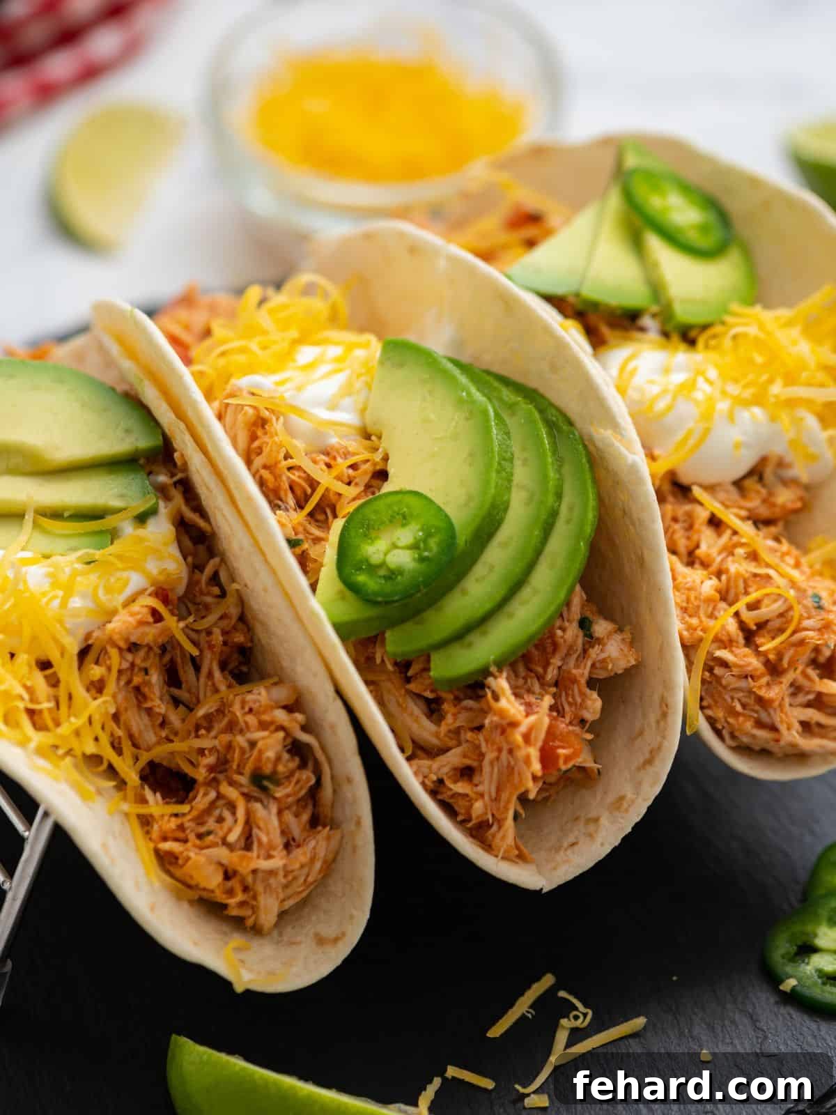 Delicious Shredded Mexican Chicken Tacos served on warm flour tortillas, generously topped with melted shredded cheese, fresh avocado slices, and a dollop of creamy sour cream.